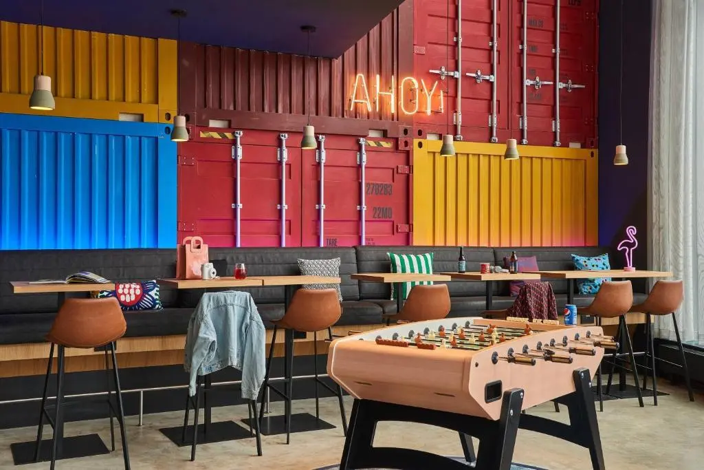 Moxy Southampton's lounge bar, with a wall of red, yellow and blue shipping containers lit by a neon 'Ahoy!' sign above bar stools and a table football