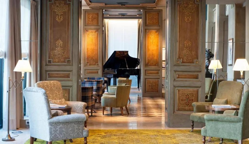 The Duquesa de Cardona lounge with painted wooden panels, armchairs in pale green and a black grand piano