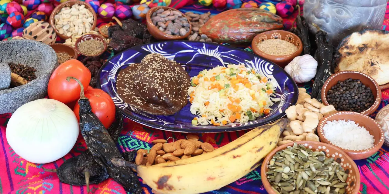 Dried chiles, cacao beans, nuts and seeds spread around a blue-and-white plate of dark mole with rice and a plantain