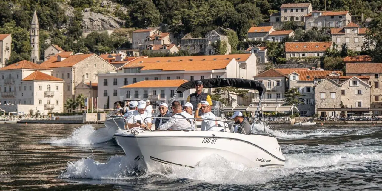 A white speedboat full of passengers in front of the stone houses of Perast's waterfront