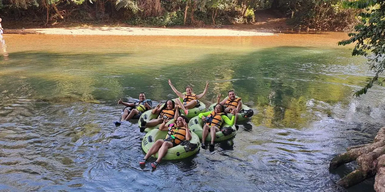 A group of smiling people in tubes and life jackets floating on a green river
