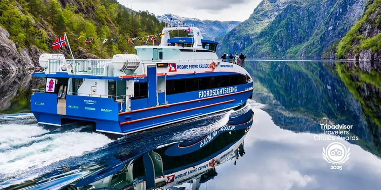 A blue-and-white catamaran cruising a calm fjord between steep green mountains