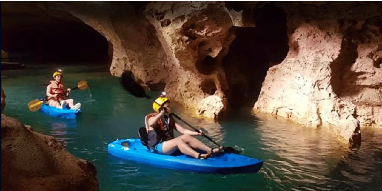 A kayaker in a helmet paddling a blue kayak inside a limestone cave