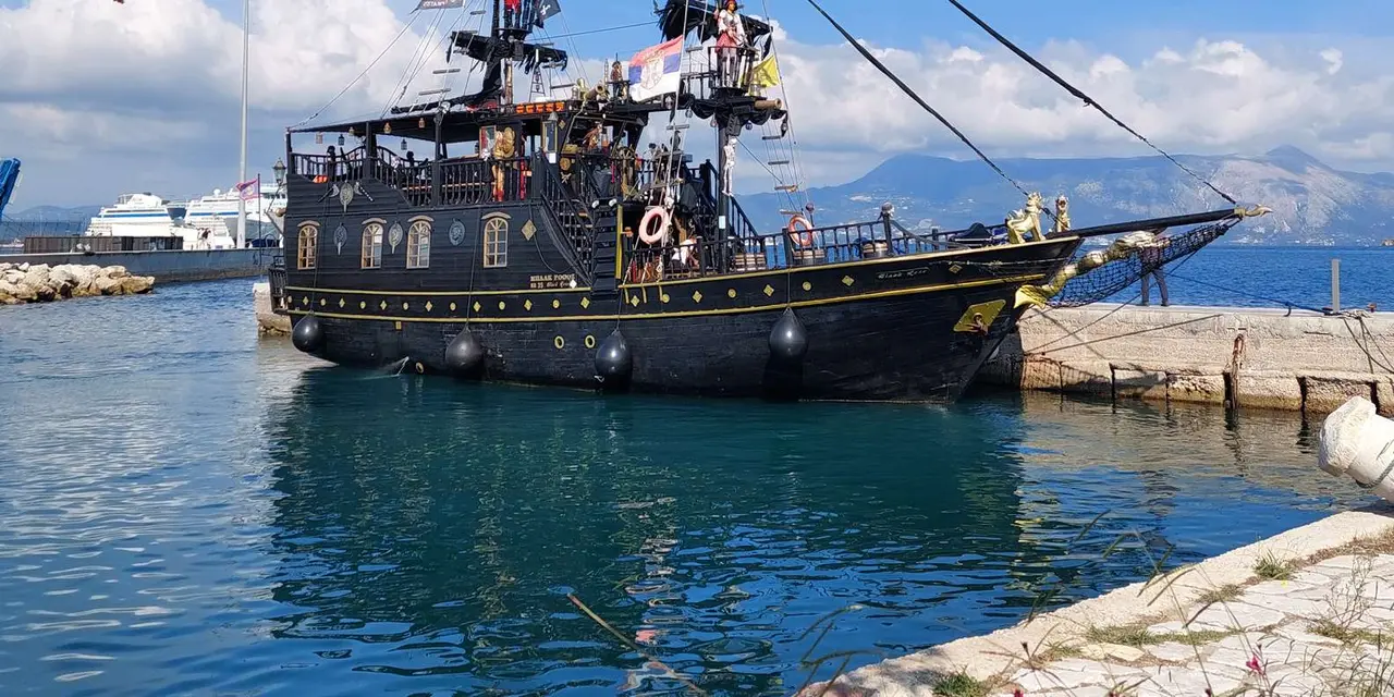 A black wooden pirate ship with tall masts moored in a calm harbour