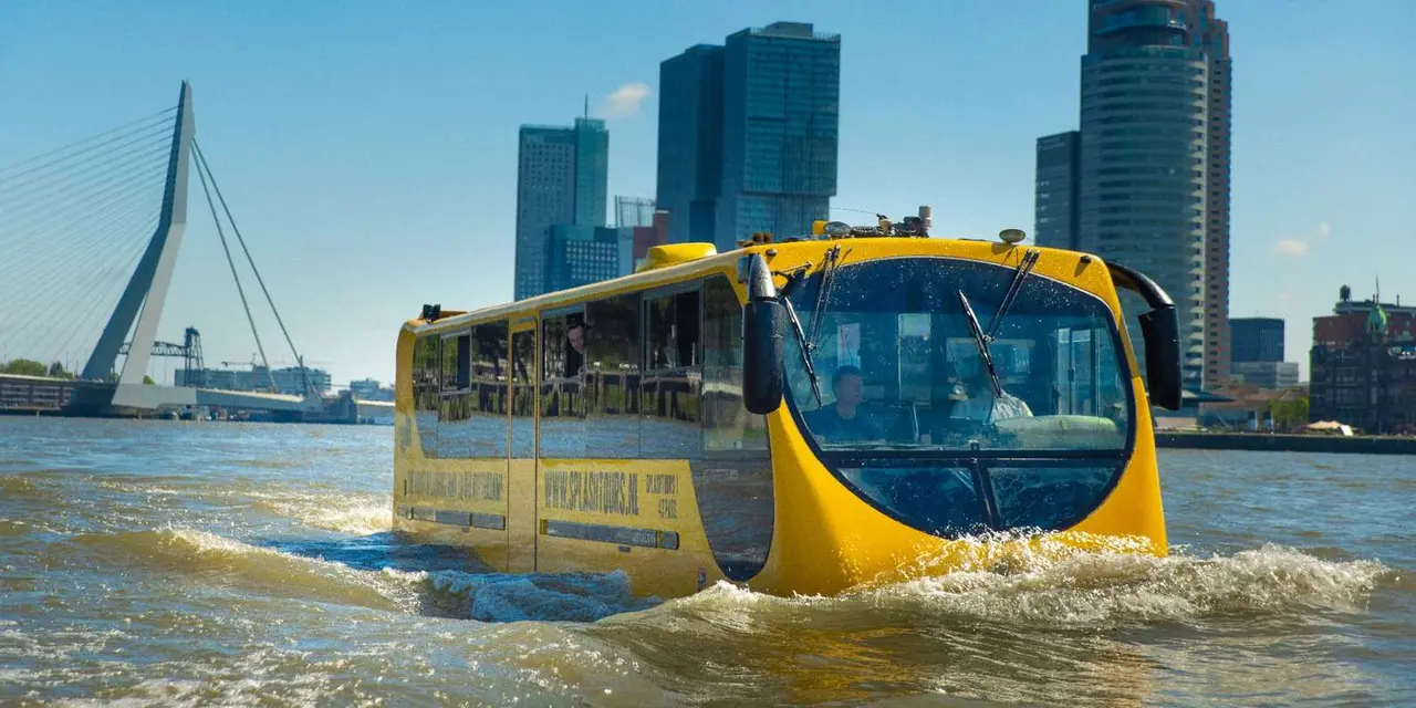 A yellow amphibious tour bus afloat on the river with the Erasmus Bridge's pylon and tall glass towers behind it on a clear day