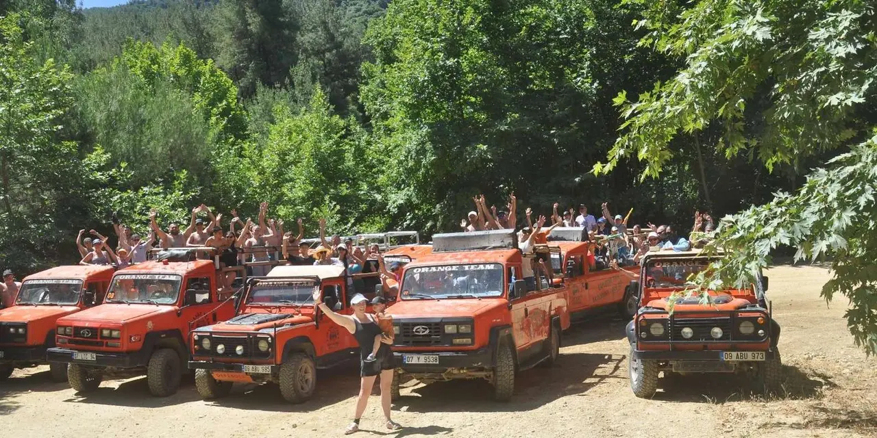A row of red Land Rover jeeps parked under green trees with a group of riders behind them