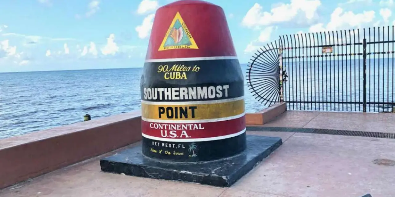 The red, black and yellow Southernmost Point buoy reading 90 Miles to Cuba, with blue sea behind it