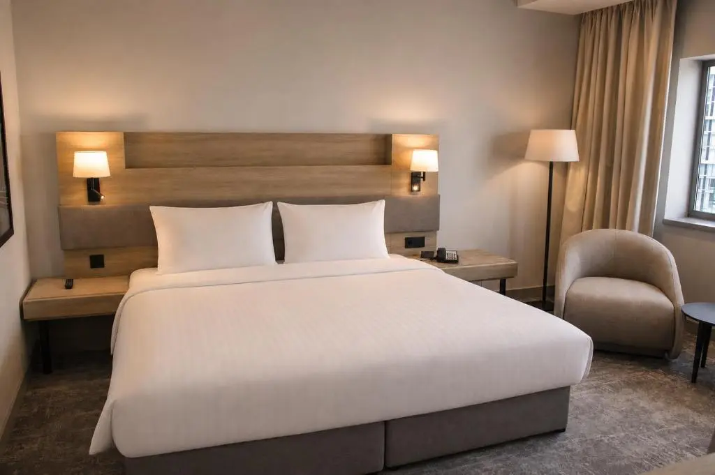 A Radisson Blu Liverpool guest room with a large white bed, bedside lamps and an armchair by the window