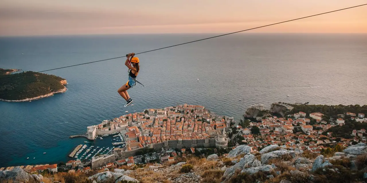 A rider on a zipline high above Dubrovnik's walled Old Town at sunset