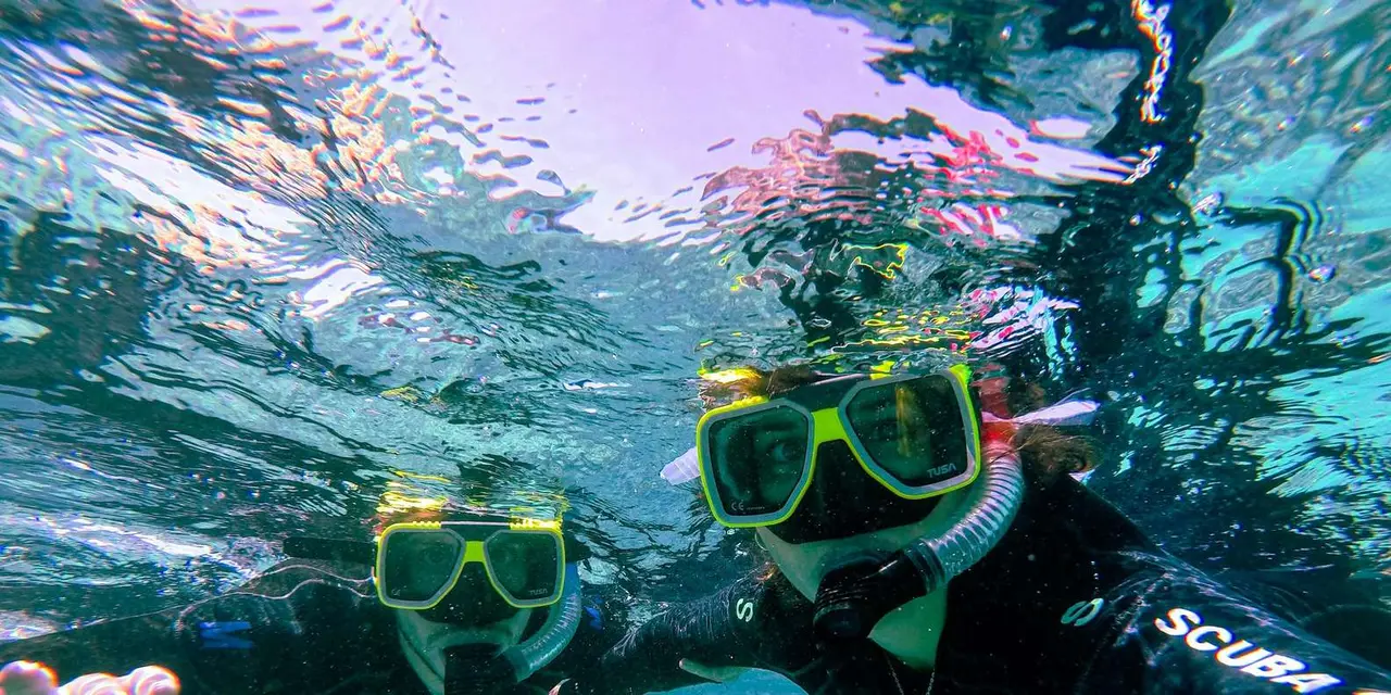 Two snorkelers in green masks smiling at the camera underwater