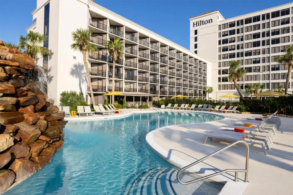 Hilton Galveston Island Resort's lagoon-style pool with a rock waterfall, lounge chairs and the balconied hotel tower behind
