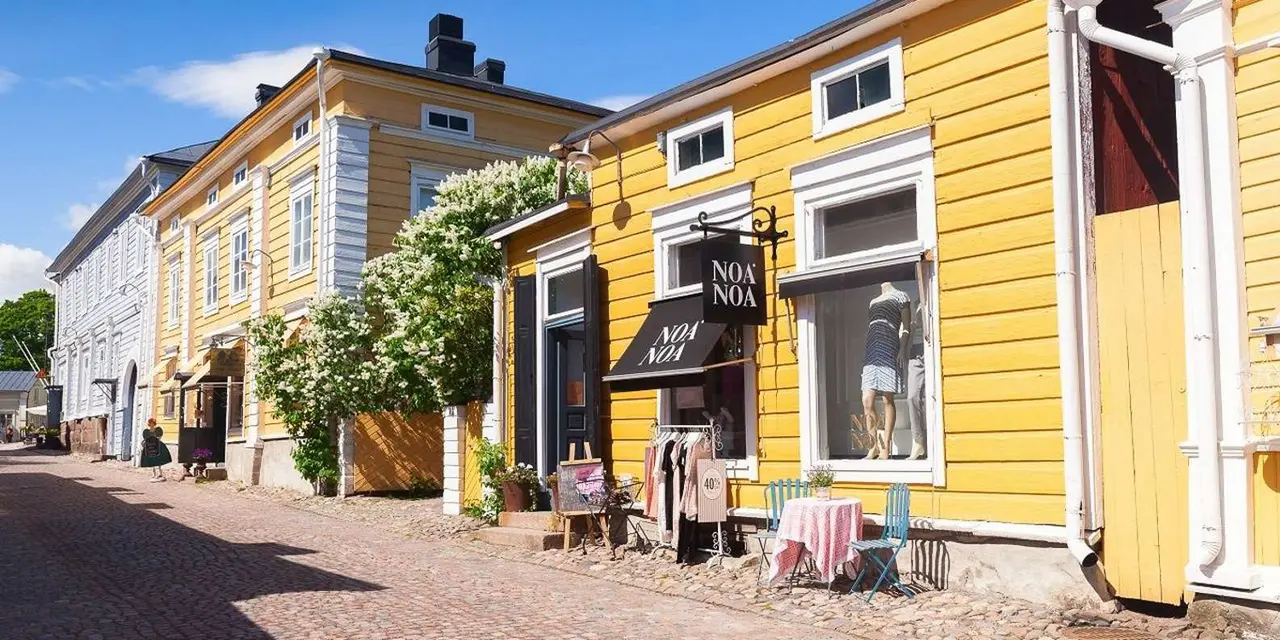 Yellow wooden Old Town houses with a boutique shopfront and flowering vines along a cobbled street in Porvoo