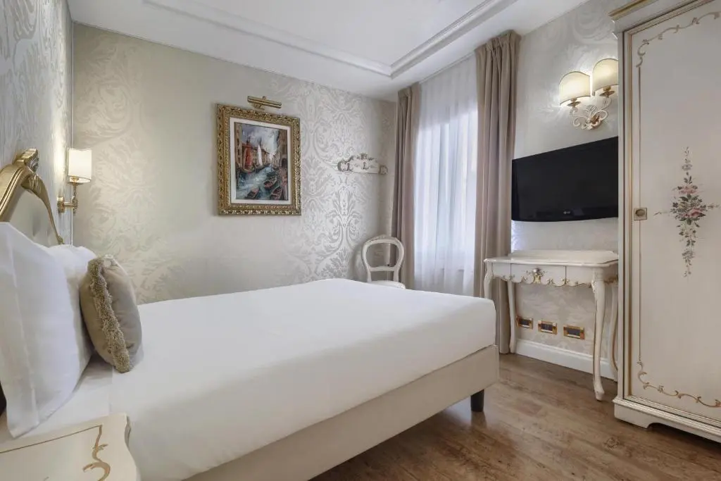 Double room at Hotel Olimpia Venice with a white bed, damask wallpaper, a gilt-framed canal painting and a painted Venetian wardrobe
