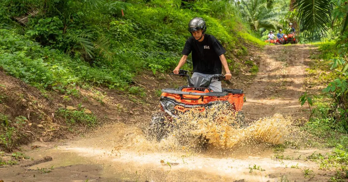 A rider on an orange ATV splashing through a muddy jungle track