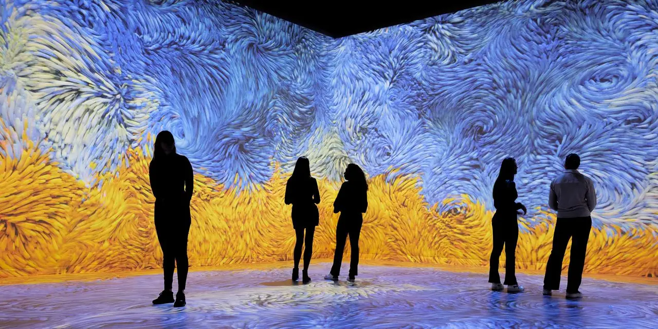 Five silhouetted visitors standing in front of a wall-to-wall projection of swirling blue and yellow brushstrokes in the style of Van Gogh