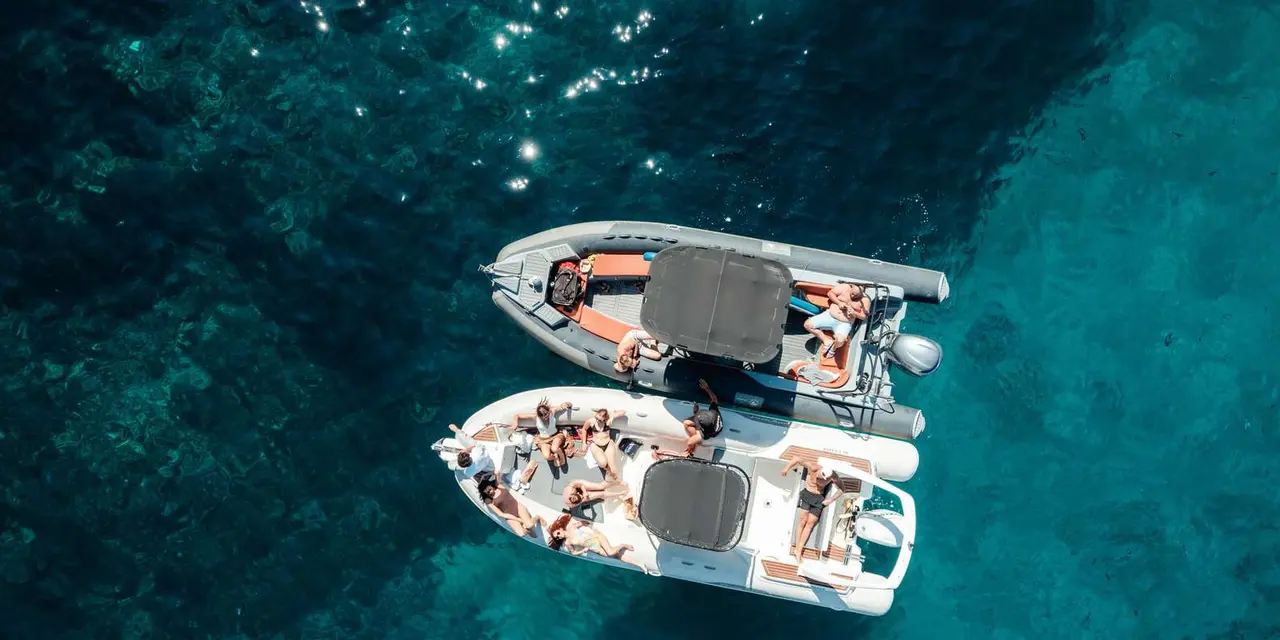 Two white semi-rigid boats with passengers seen from above on turquoise water