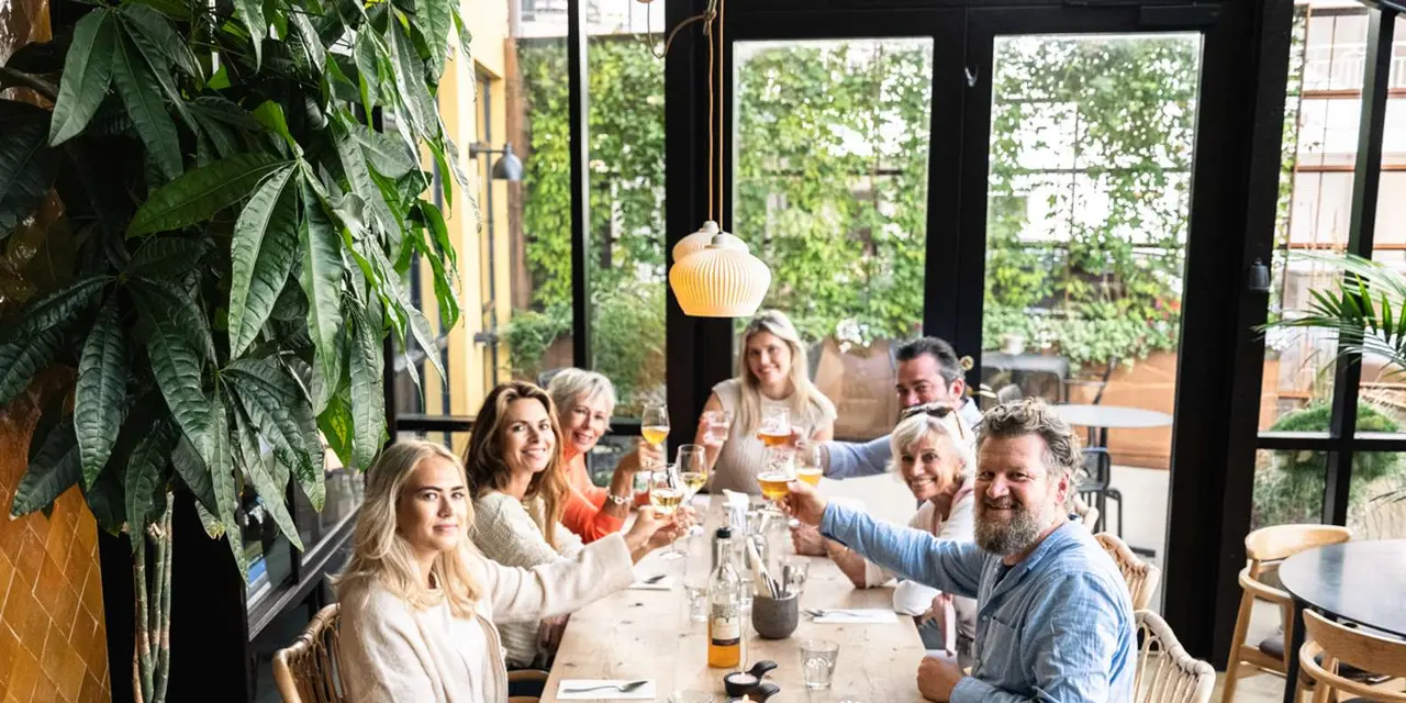 A group of friends raising glasses around a long wooden table in a bright restaurant