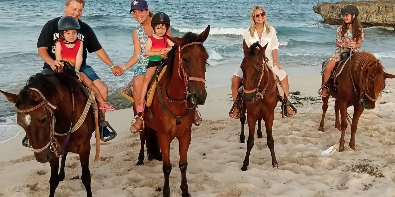 Riders on horses standing on a sandy beach with waves breaking behind them
