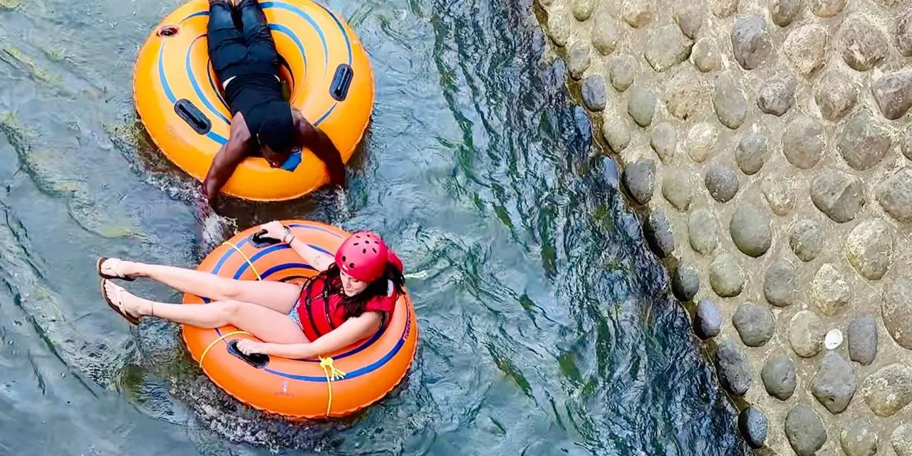 Two people floating down a jungle river in bright orange inner tubes