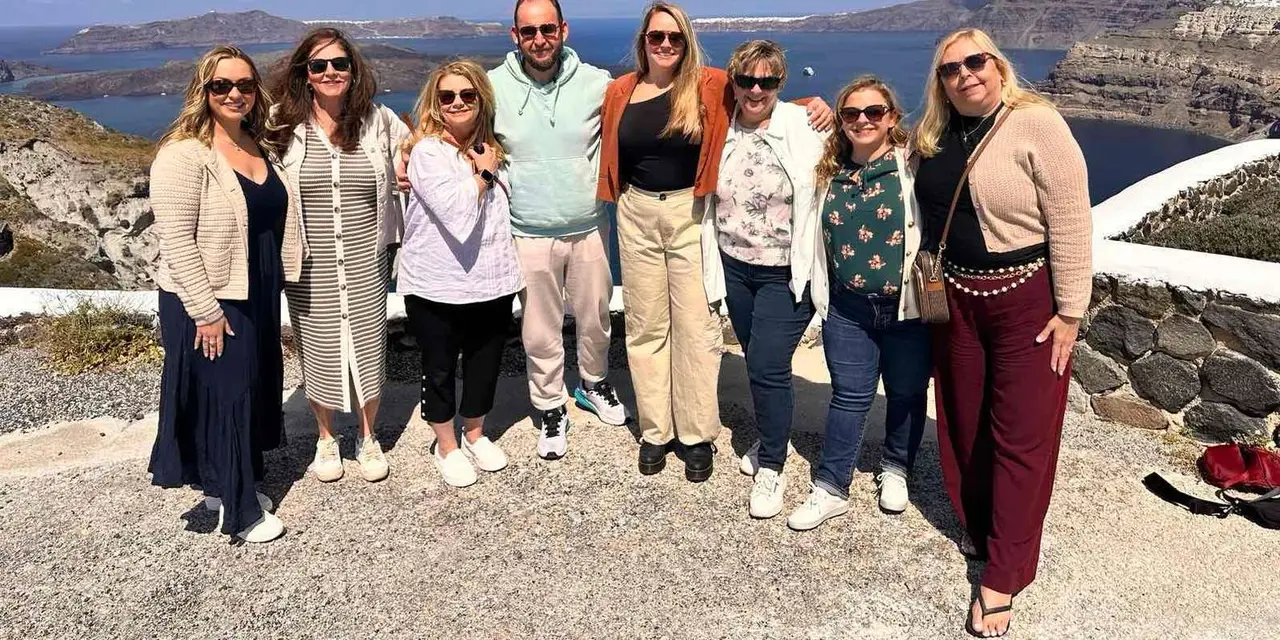 Eight visitors posing on a gravel viewpoint with the caldera and volcanic islands behind them
