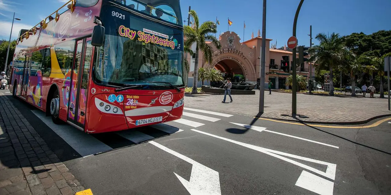 A red open-top sightseeing bus on a street in front of the arched entrance of the Mercado de Nuestra Señora de África