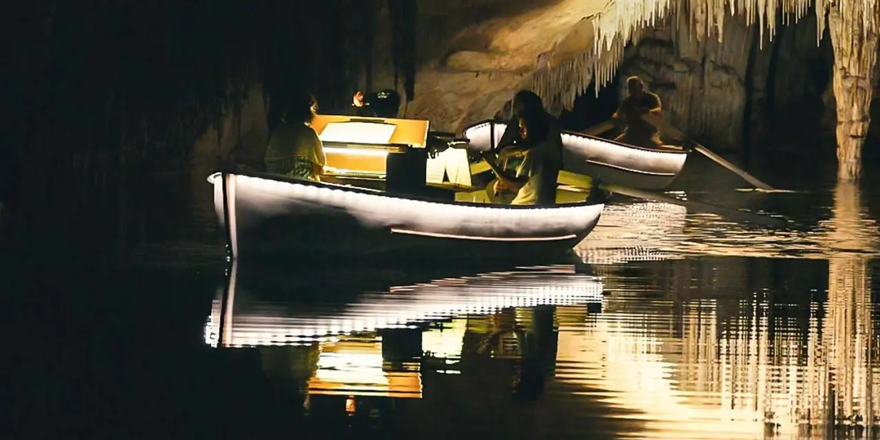 Wooden boats on the lit underground lake inside the Caves of Drach with stalactites above