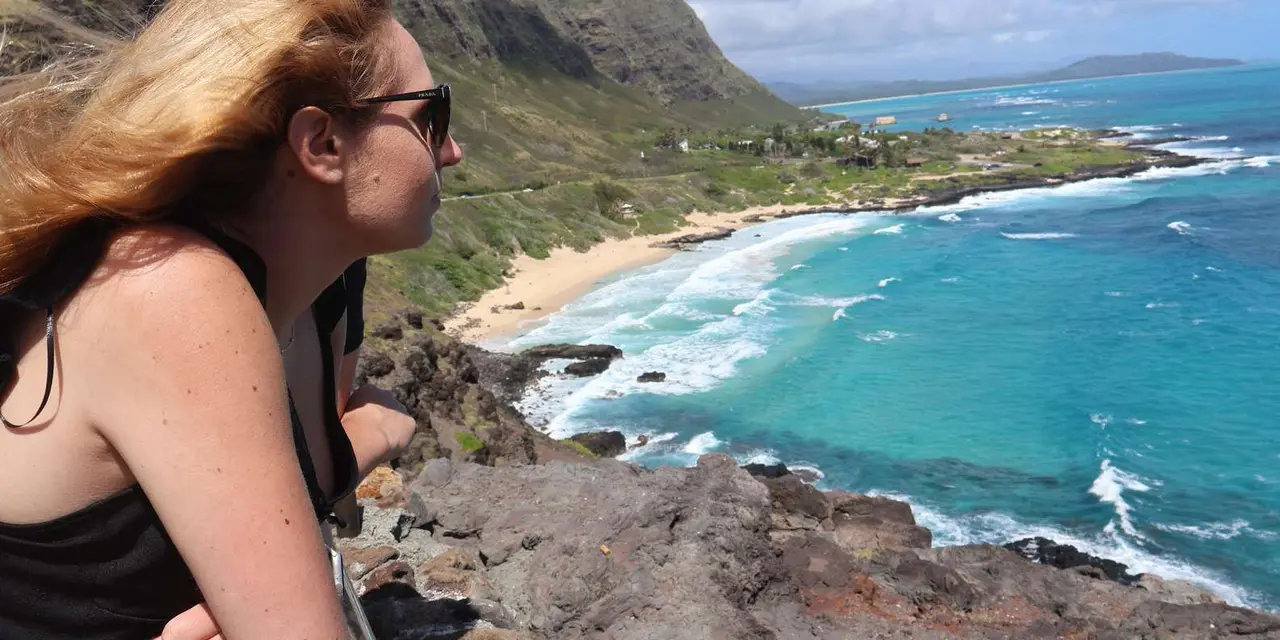 A woman with windblown hair looking over a cliff-backed cove of turquoise water