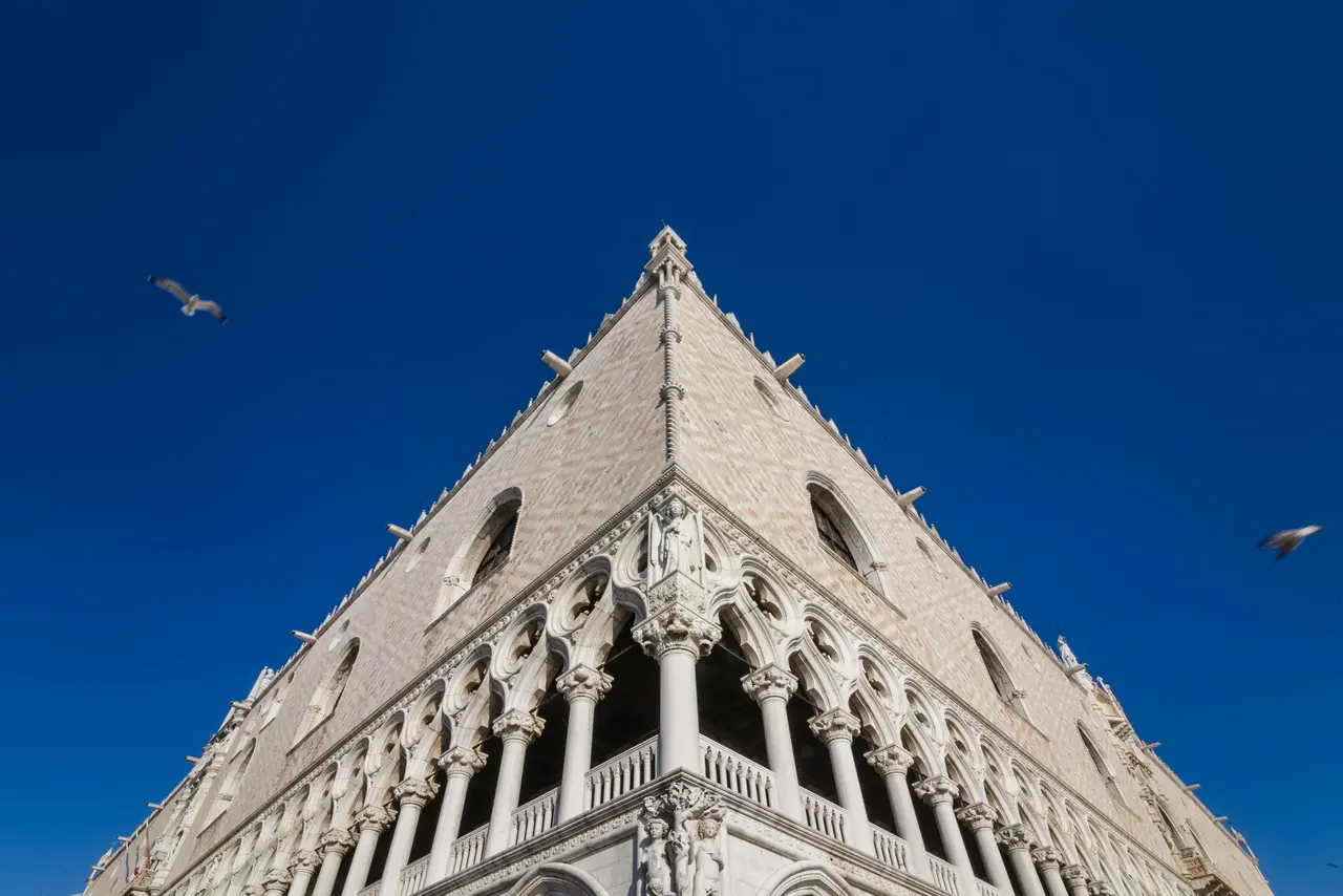 The corner of the Doge's Palace's white and pink facade against a deep blue sky