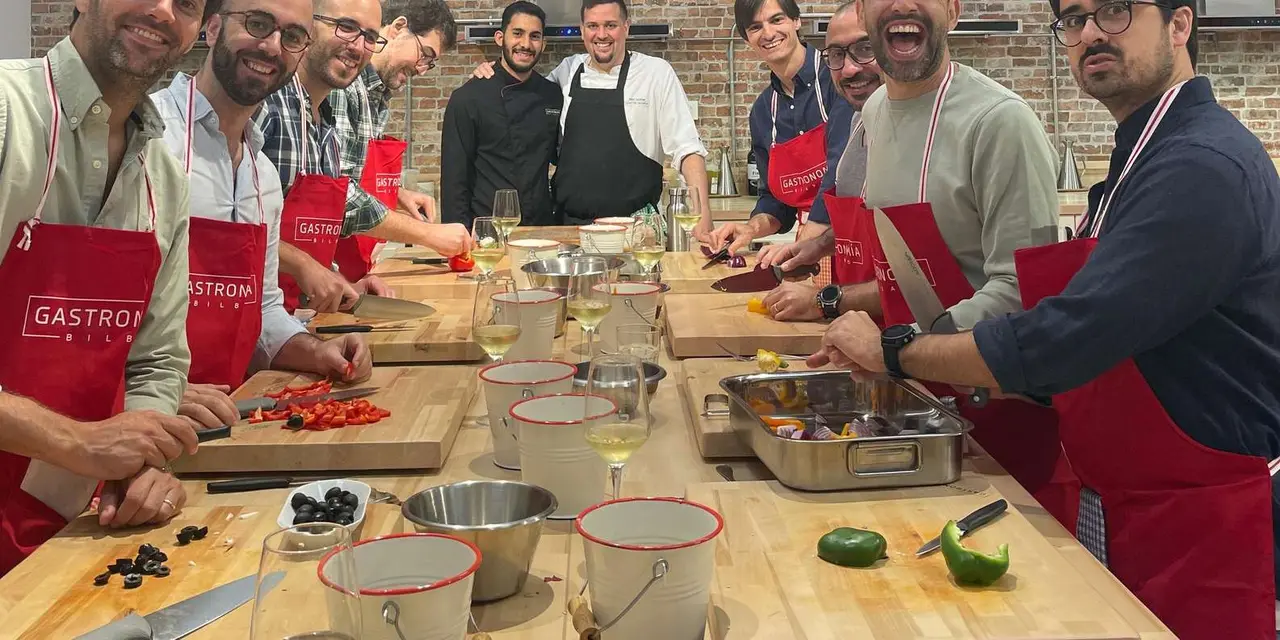 A row of people in red aprons chopping vegetables at a long wooden counter with a chef smiling behind them