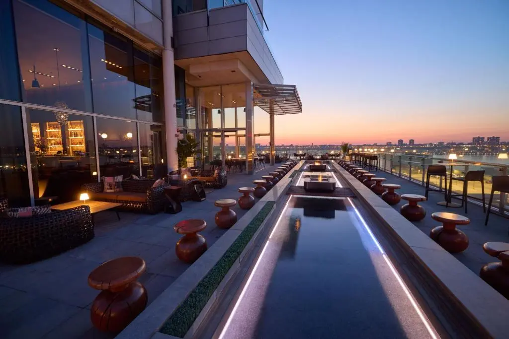 Ink 48's rooftop terrace at dusk, with a lit reflecting pool, low seats and the Hudson River and New Jersey skyline beyond