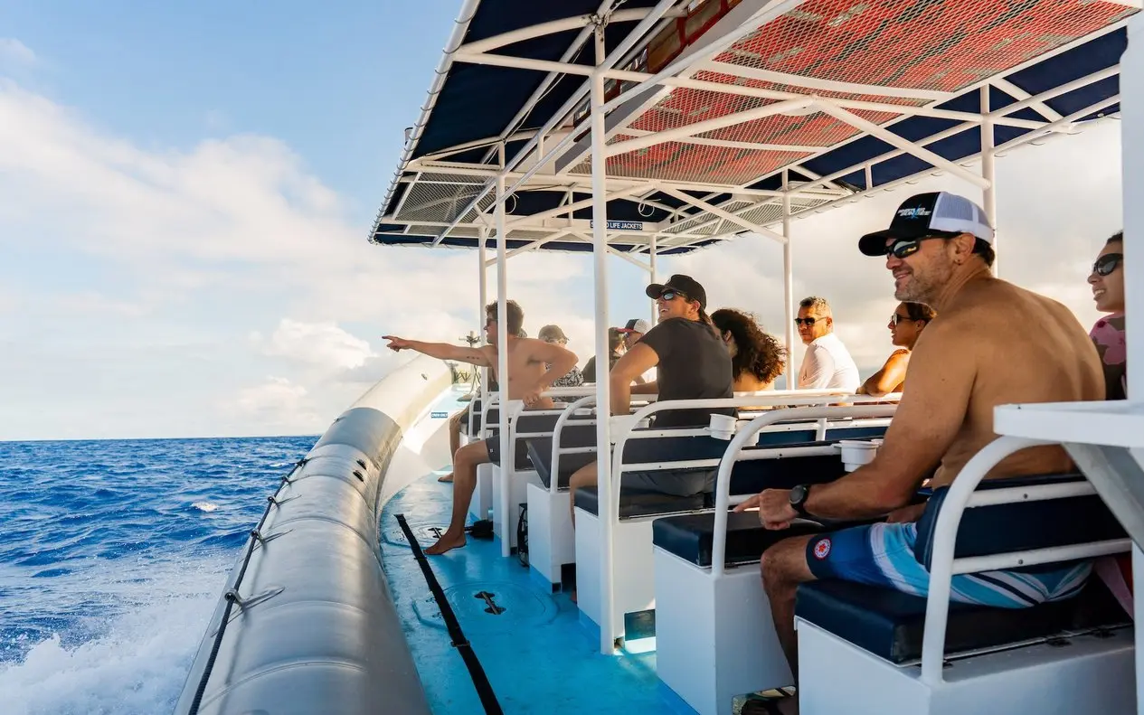Snorkelers seated under the canopy of a big inflatable raft speeding across blue water