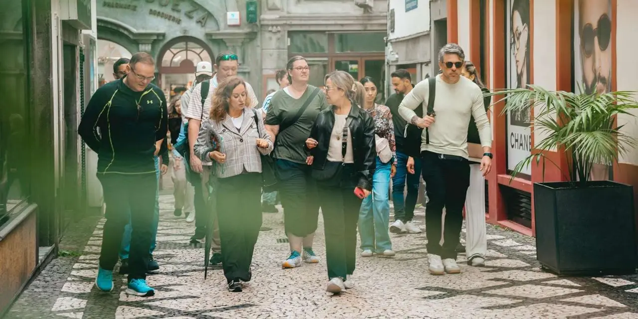 A group of visitors walking together along a cobbled lane lined with shopfronts in central Funchal