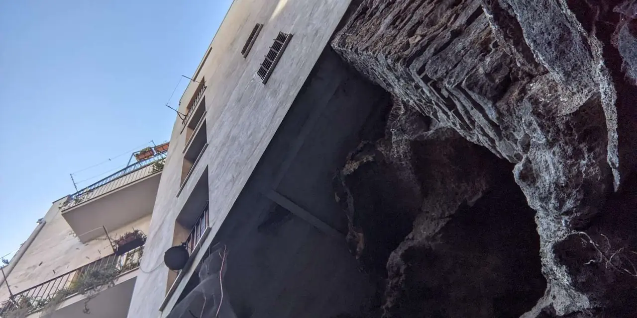 A pale building wall in Catania with a dark opening in the lava stone beside it