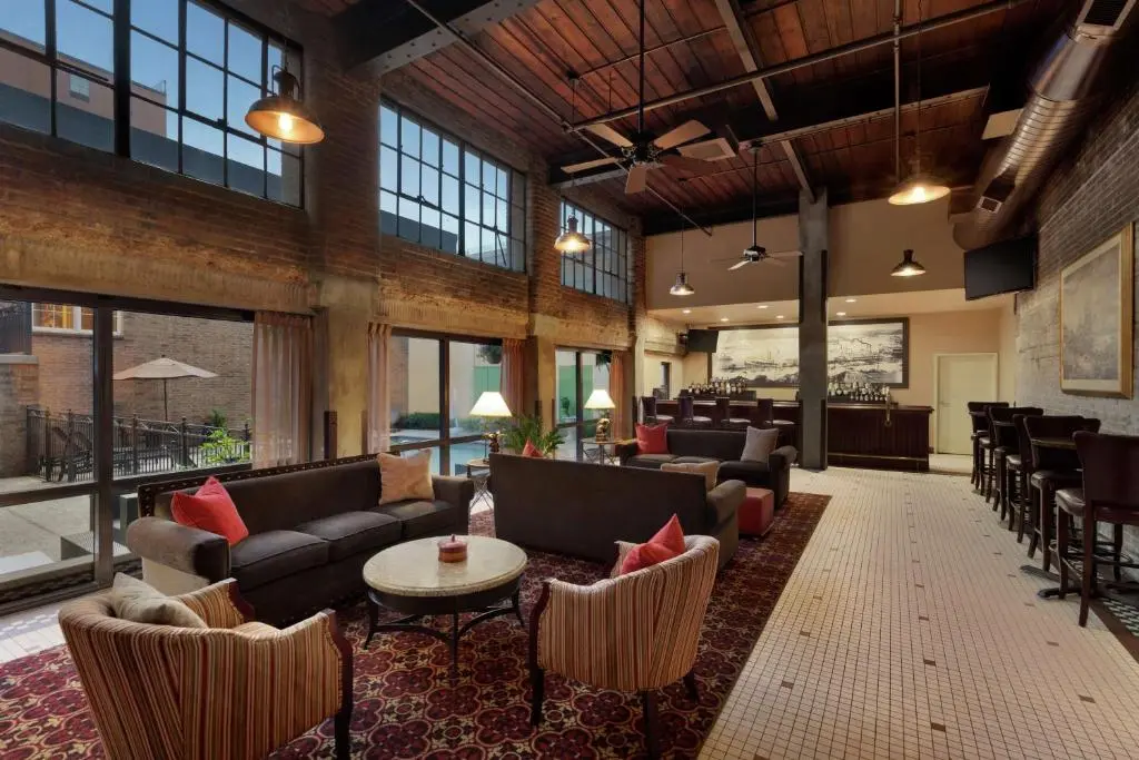 The Hampton Inn lobby in a converted warehouse: exposed brick, tall windows, a red-patterned rug and sofas, with a bar at the back