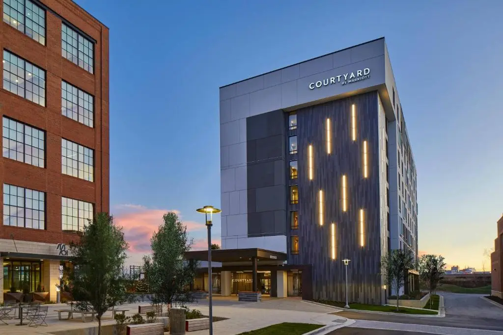 The Courtyard by Marriott Baltimore Downtown/McHenry Row at dusk, a modern building with lit vertical panels beside a brick building with a plaza and trees