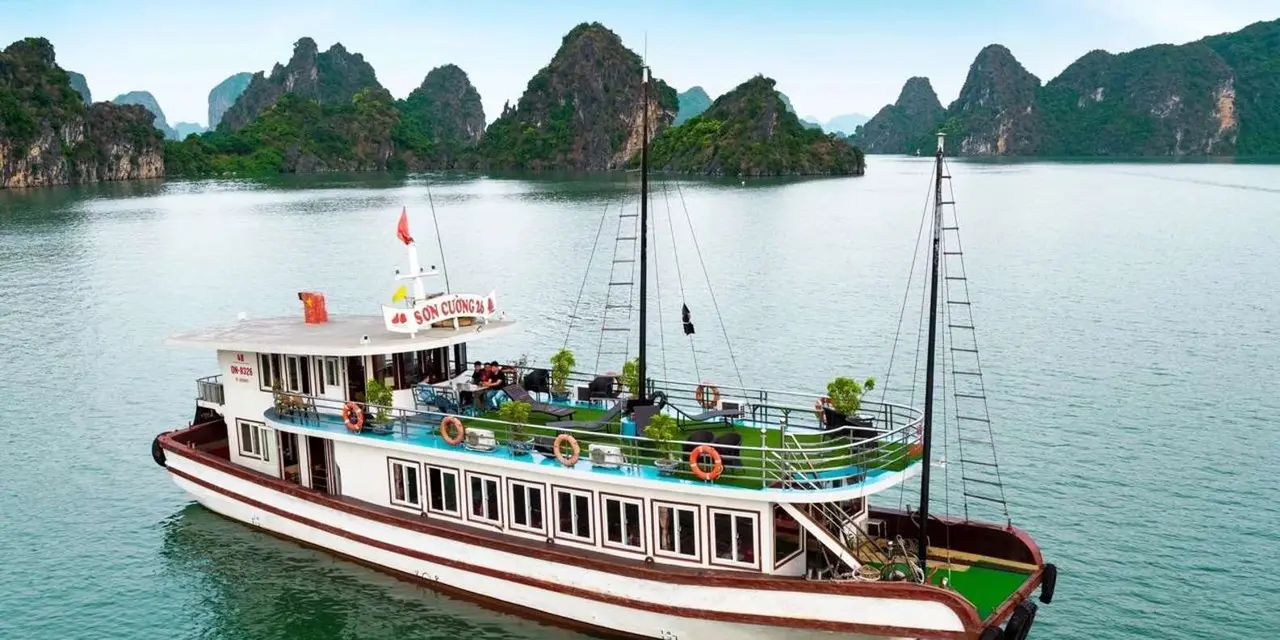 A white and brown wooden tour boat on calm green water with forested limestone islands behind it