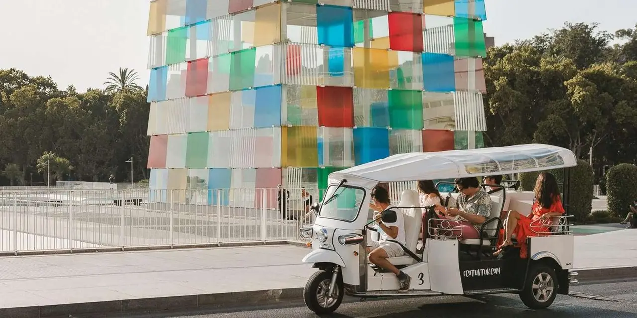 An electric tuk tuk parked beside the multicoloured glass cube of the Centre Pompidou on Málaga's waterfront