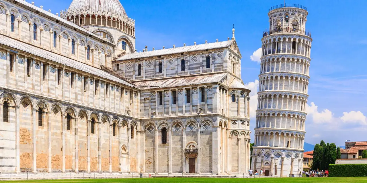 Pisa's cathedral and the Leaning Tower rising from the green lawn of the Piazza dei Miracoli under a blue sky