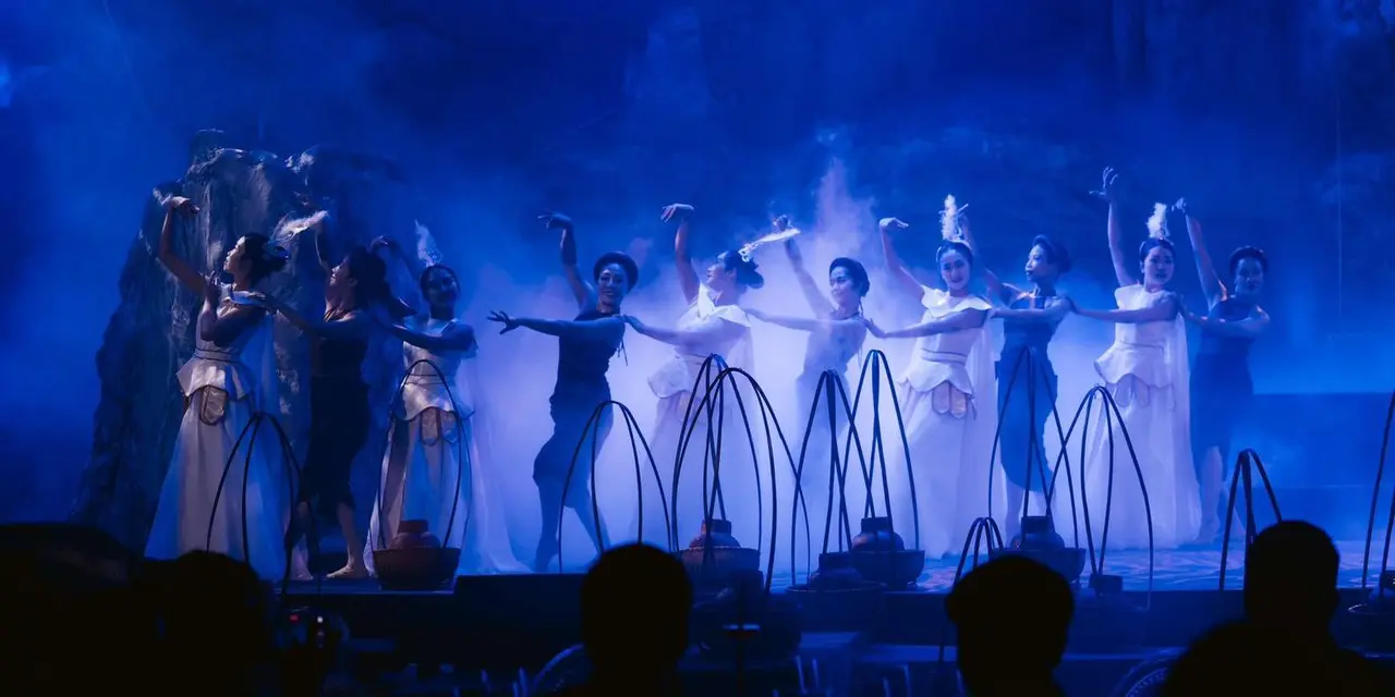 A row of performers in white and blue costumes on a stage filled with blue haze, the Dragon Pearl Cave show