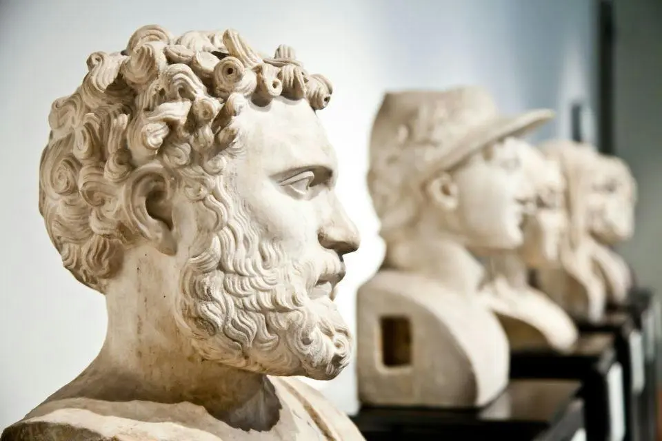 A row of white marble portrait busts on plinths in a bright museum gallery