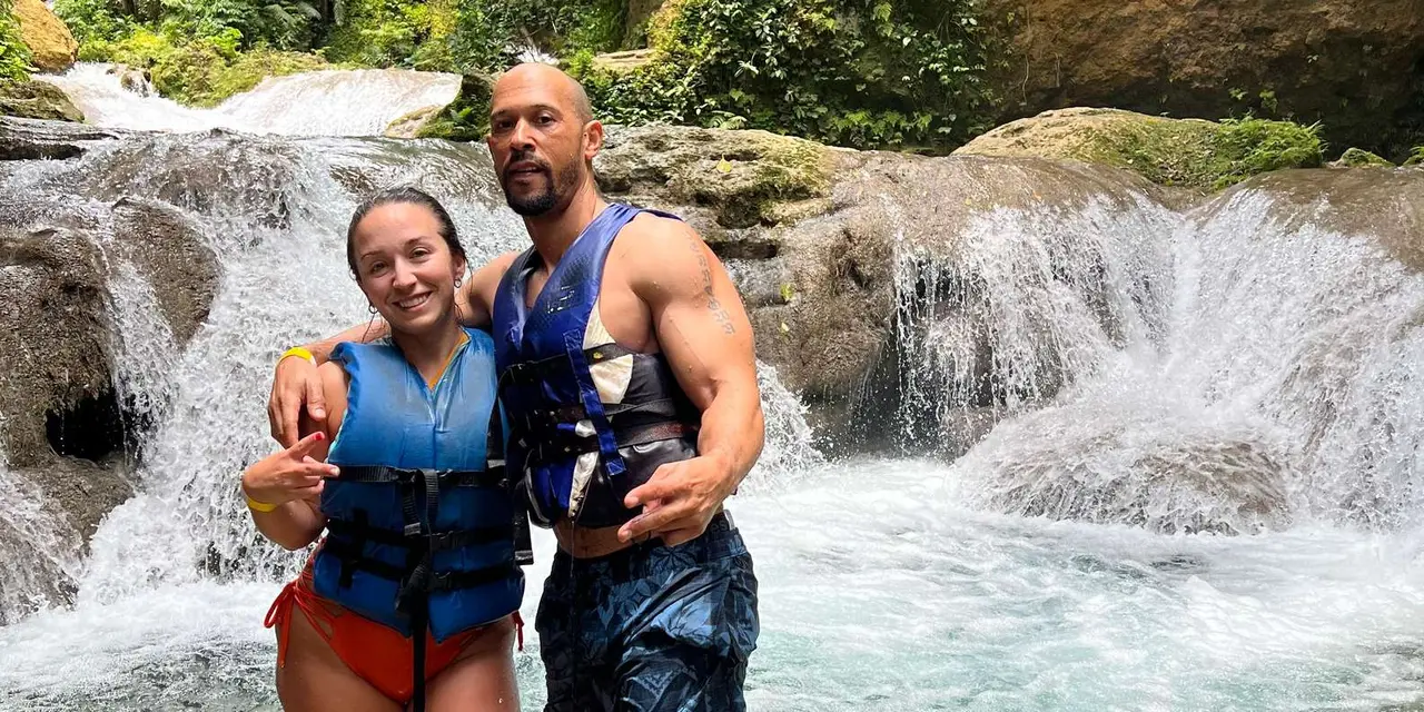 A couple in life vests standing in front of a cascading waterfall