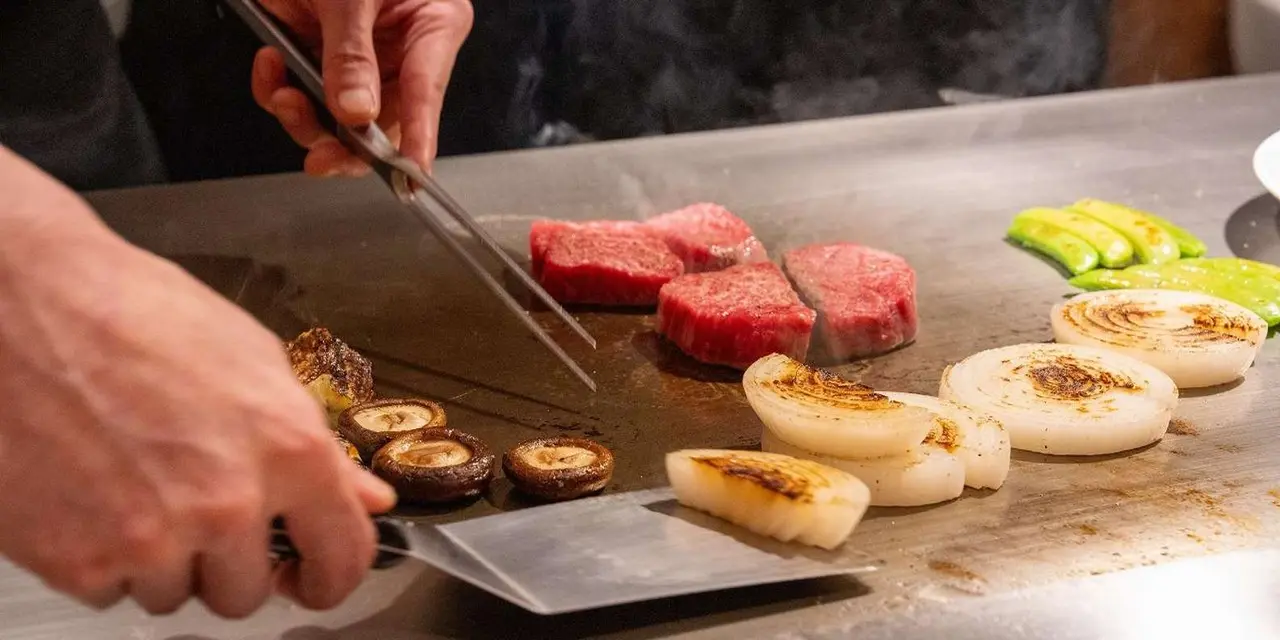 A chef searing marbled Kobe beef and vegetables on a teppan grill