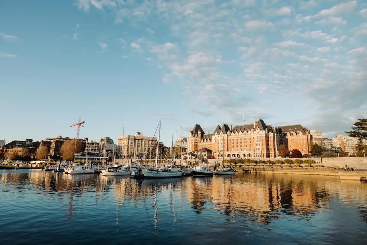 The Fairmont Empress and downtown Victoria across the calm Inner Harbour, with moored sailboats and their reflections under a soft blue sky