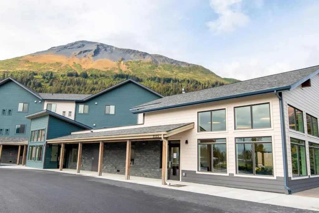 The Seward Gateway Hotel's grey-green and cream buildings with a covered entrance, below a green mountainside