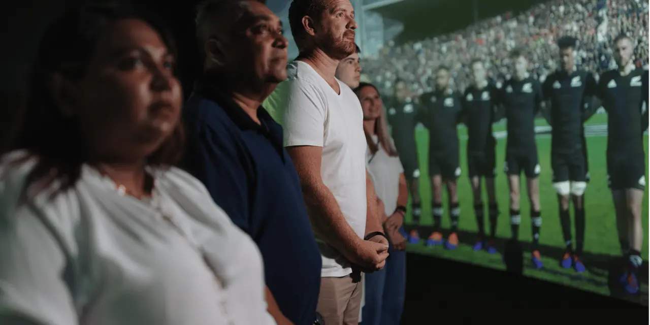 Visitors standing in front of a wide curved screen showing the All Blacks performing the haka