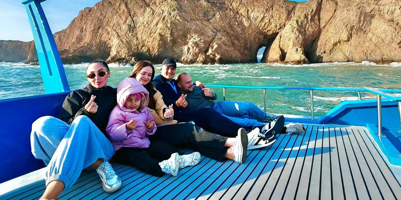 A family on a boat deck below golden sea cliffs