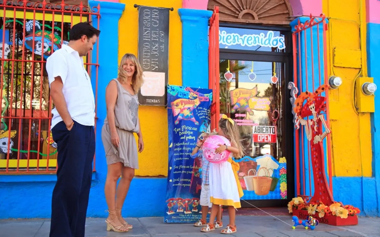 A woman and a girl outside a brightly painted craft shop with a Bienvenidos sign