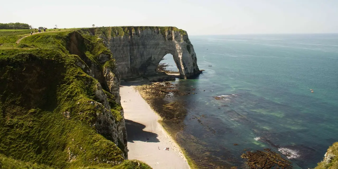 A natural rock arch in white cliffs above a pebble beach and a green-blue sea at Étretat
