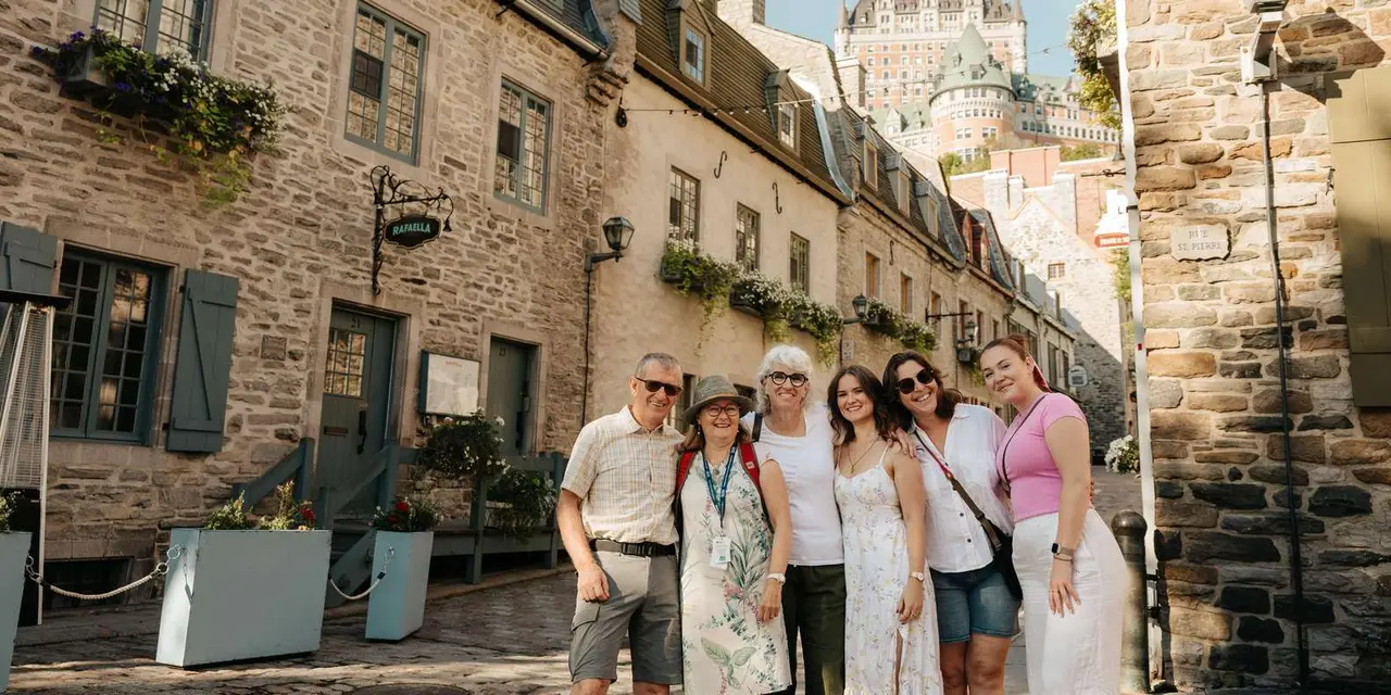 A smiling tour group on a stone street in Old Québec with the Château Frontenac's tower behind them