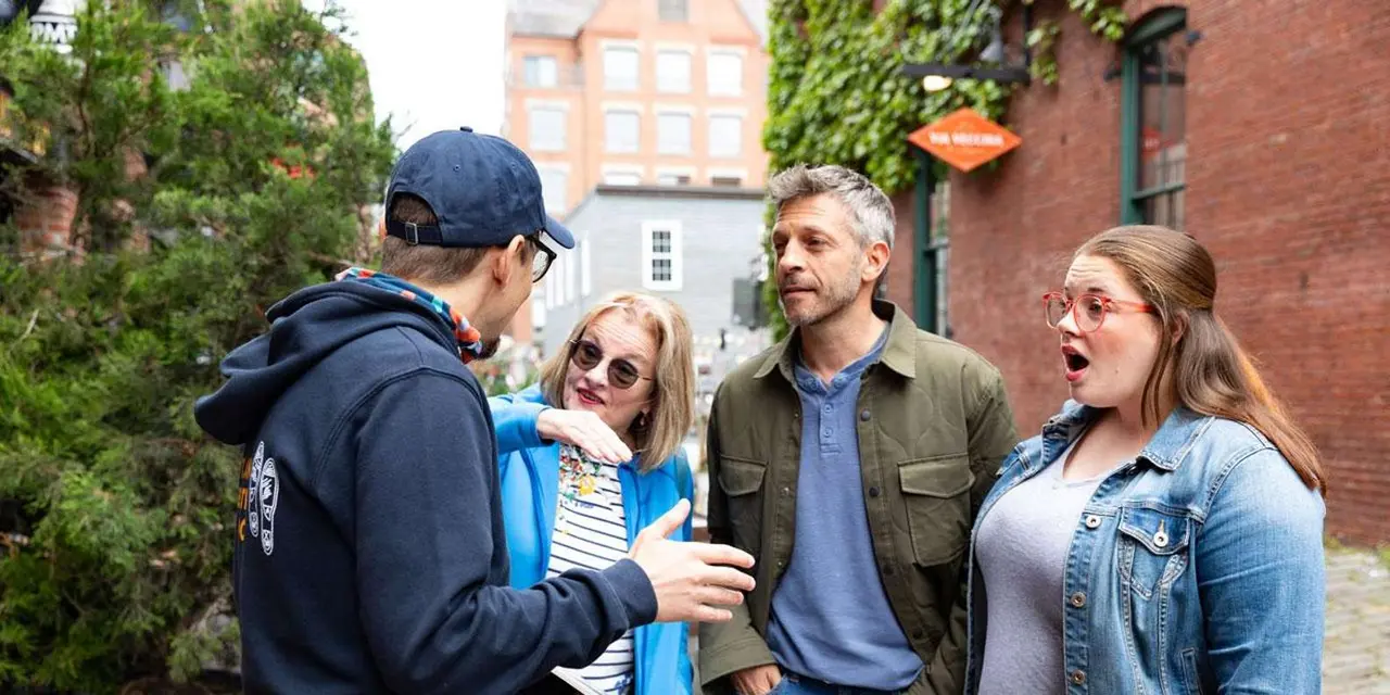 A guide talking with three guests in front of old brick buildings in Portland's Old Port